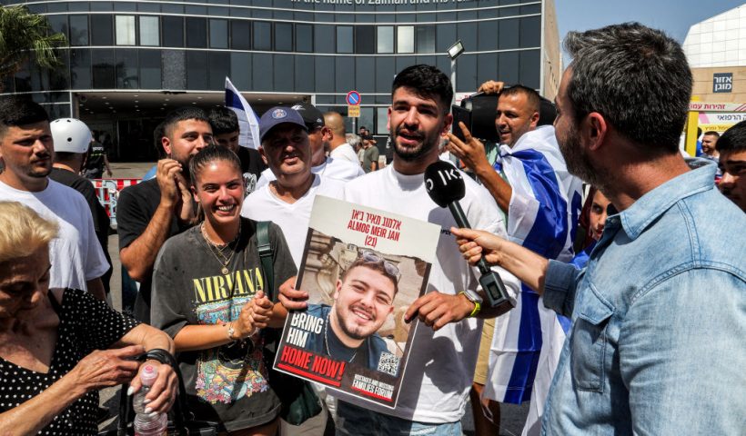 Friends of Almog Meir Jan, one of the four Israeli hostages that were rescued from captivity in the Gaza Strip since the October 7 attacks, pose for a photo with his picture as they gather with others outside Sheba Tel-HaShomer Medical Centre after the hostages were transferred there, in Ramat Gan on June 8, 2024 amid the ongoing conflict in the Palestinian territory between Israel and the militant group Hamas. Israel said its forces rescued four hostages alive from a Gaza refugee camp on June 8 as it intensified an assault despite scrutiny over a deadly strike on a UN-run school there. The four had been kidnapped by Hamas from the Nova music festival during the October 7 attacks that sparked the war, the army said. (Photo by JACK GUEZ / AFP) (Photo by JACK GUEZ/AFP via Getty Images)