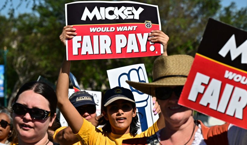 Disney employees hold up signs as they rally outside the main entrance of Disneyland Resort in Anaheim, California, on July 17, 2024, ahead of a planned strike authorization vote. More than 200 Disneyland Resort employees protested outside the world-famous California theme parks July 17, calling for better wages and denouncing alleged anti-union practices by the company ahead of a looming strike vote. Featuring workers in costumes from the parks' "Indiana Jones" and "Star Wars" themed rides, among others, the rally was organized by unions representing some 14,000 Disneyland employees, from rollercoaster operators to candy makers. (Photo by Frederic J. BROWN / AFP) (Photo by FREDERIC J. BROWN/AFP via Getty Images)