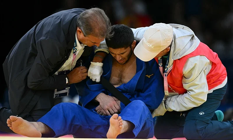 Tajikistan's Nurali Emomali receives medical treatment during the judo men's -66kg quarter-final bout of the Paris 2024 Olympic Games at the Champ-de-Mars Arena, in Paris on July 28, 2024. (Photo by Luis ROBAYO / AFP) (Photo by LUIS ROBAYO/AFP via Getty Images)