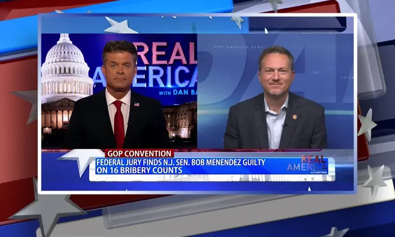 Video still from Real America on One America News Network showing a split screen of the host on the left side, and on the right side is the guest, Rep. Michael Cloud.