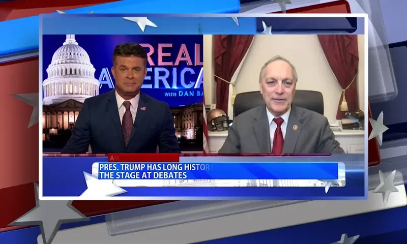 Video still from Real America on One America News Network showing a split screen of the host on the left side, and on the right side is the guest, Rep. Andy Biggs.
