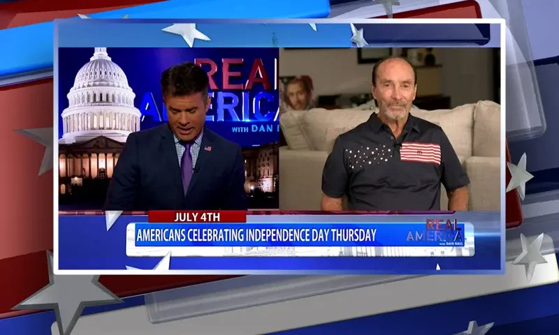 Video still from Real America on One America News Network showing a split screen of the host on the left side, and on the right side is the guest, Lee Greenwood.