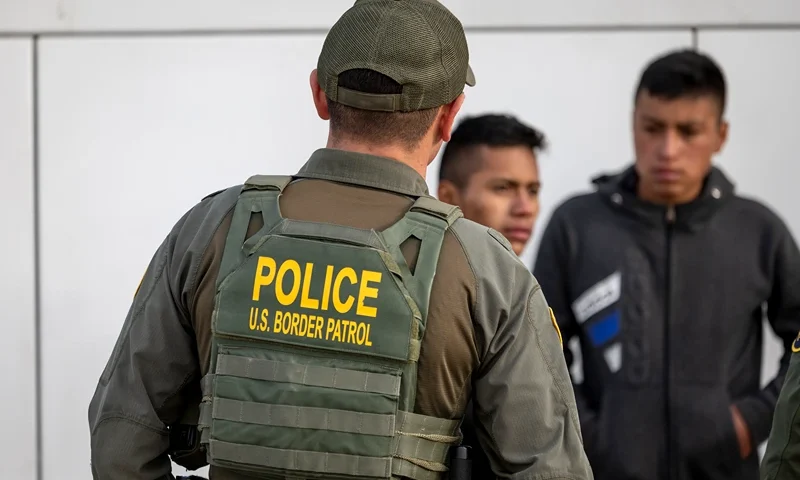 EAGLE PASS, TEXAS - JANUARY 07: A U.S. Border Patrol agent watches as immigrants prepare to board a bus after crossing the U.S.-Mexico border on January 07, 2024 in Eagle Pass, Texas. According the a new report released by U.S. Department of Homeland Security, some 2.3 million migrants, mostly from families seeking asylum, have been released into the U.S. under the Biden Administration since 2021. (Photo by John Moore/Getty Images)