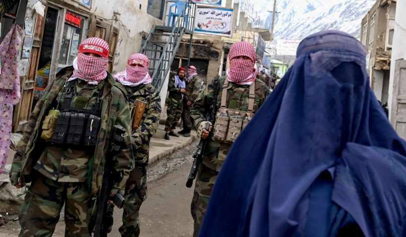 TOPSHOT - Taliban security personnel stand guard as an Afghan burqa-clad woman (R) walks along a street at a market in the Baharak district of Badakhshan province on February 26, 2024. (Photo by Wakil KOHSAR / AFP) (Photo by WAKIL KOHSAR/AFP via Getty Images)