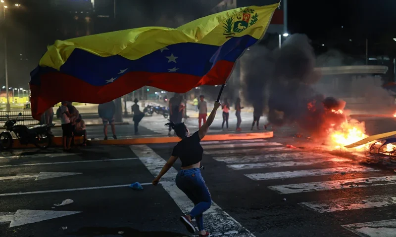 CARACAS, VENEZUELA - JULY 29: A protester runs waving a Venezuelan flag during a protest against the official results of the presidential election on July 29, 2024 in Caracas, Venezuela. Incumbent president Maduro was announced as the winner of a controversial presidential election with the 51,20% of the votes while opposition candidate Edmundo Gonzalez of the Plataforma Unitaria Democr·tica Coalition got the 44,2% according to the 'Consejo Nacional Electoral' CNE (National Electoral Council) (Photo by Jesus Vargas/Getty Images)