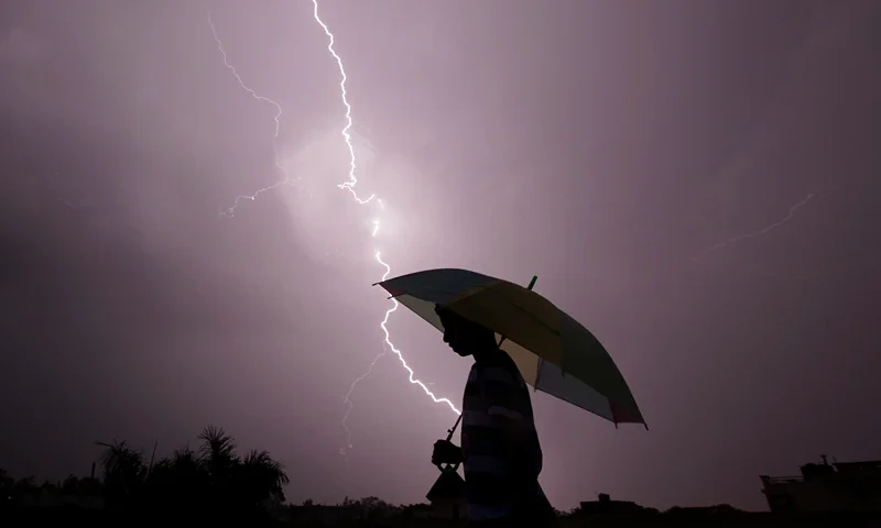 TOPSHOT - A pedestrian walks with an umbrella as lightning strikes during an evening thunderstorm in Jammu on May 14, 2015. AFP PHOTO / RAKESH BAKSHI (Photo by rakesh bakshi / AFP) (Photo by RAKESH BAKSHI/AFP via Getty Images)