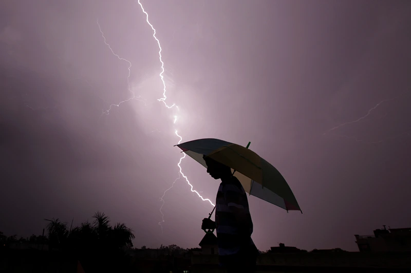 TOPSHOT - A pedestrian walks with an umbrella as lightning strikes during an evening thunderstorm in Jammu on May 14, 2015. AFP PHOTO / RAKESH BAKSHI (Photo by rakesh bakshi / AFP) (Photo by RAKESH BAKSHI/AFP via Getty Images)