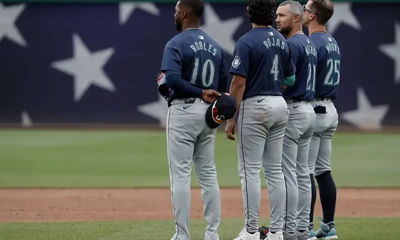 Seattle Mariners center fielder Victor Robles (10) and third baseman Josh Rojas (4) and first base coach Kristopher Negr—n (21) and second baseman Dylan Moore (25) stand for the playing of God Bless America during the seventh inning stretch against the Pittsburgh Pirates at PNC Park. Mandatory Credit: Charles LeClaire-USA TODAY Sports