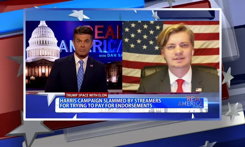 Video still from Real America on One America News Network showing a split screen of the host on the left side, and on the right side is the guest, Alex Stone.