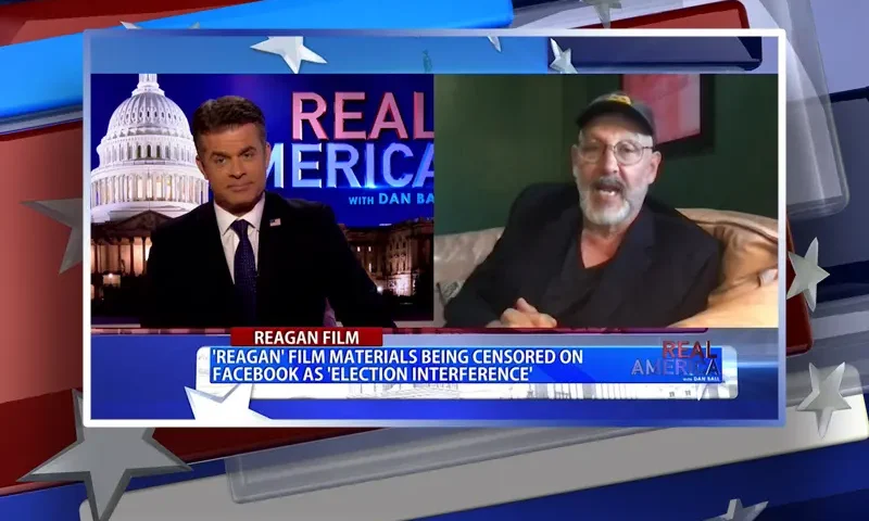 Video still from Real America on One America News Network showing a split screen of the host on the left side, and on the right side is the guest, Nick Searcy.