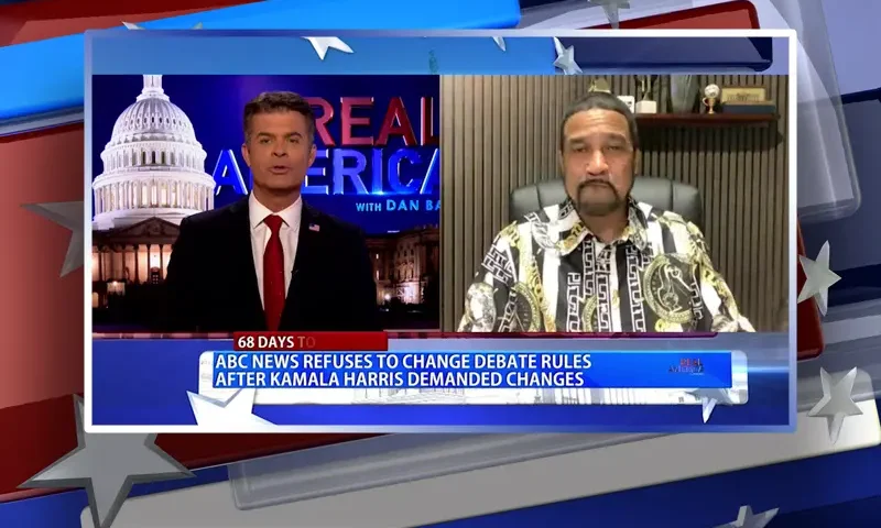 Video still from Real America on One America News Network showing a split screen of the host on the left side, and on the right side is the guest, Dr. Darrell Scott.