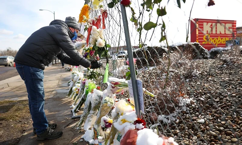 A man places flowers in the fence at a makeshift memorial for the victims of a mass shooting outside a King Soopers grocery store on March 24, 2021 in Boulder, Colorado. Ten people, including a police officer, were killed in the shooting on Monday.(Photo by Michael Ciaglo/Getty Images)