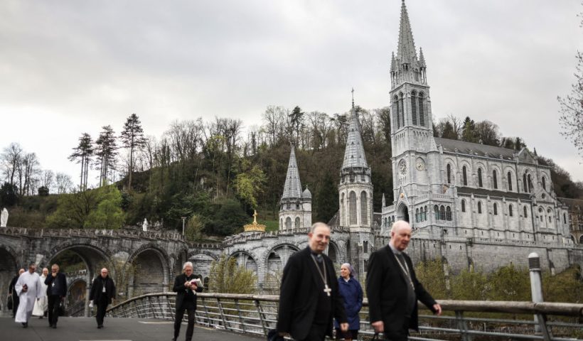 Bishops and archbishops walk near the Notre-Dame-du-Rosaire Basilica and the Immaculate Conception Basilica (both seen in the background) in the Sanctuary of Lourdes, in Lourdes, southwestern France, on March 31, 2023. (Photo by Charly TRIBALLEAU / AFP) (Photo by CHARLY TRIBALLEAU/AFP via Getty Images)