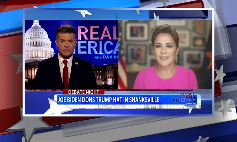 Video still from Real America on One America News Network showing a split screen of the host on the left side, and on the right side is the guest, Kari Lake.