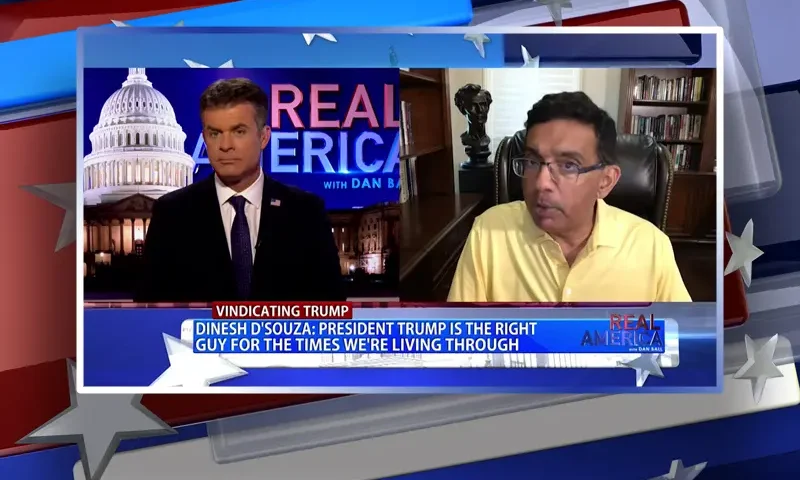 Video still from Real America on One America News Network showing a split screen of the host on the left side, and on the right side is the guest, Dinesh D'Souza.