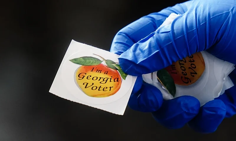 ATLANTA, GA - JUNE 09: A polling place worker holds an "I'm a Georgia Voter" sticker to hand to a voter on June 9, 2020 in Atlanta, Georgia. Georgia, West Virginia, South Carolina, North Dakota, and Nevada are holding primaries amid the coronavirus pandemic. (Photo by Elijah Nouvelage/Getty Images)