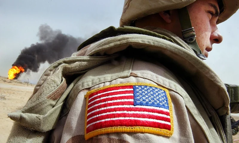 RUMAYLA, IRAQ - MARCH 27: U.S. Army Specialist Chad Morton, of George West, Texa,s stands next to a burning oil well at the Rumayla oil fields March 27, 2003 in Rumayla, Iraq. Several oil wells were set ablaze by retreating Iraqi troops in the Ramayla area, the second largest offshore oilfield in the country, near the Kuwaiti border. (Photo by Mario Tama/Getty Images)