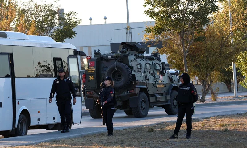 Turkish police officers gather as an armed personnel vehicle drives along a road in Kahramankazan, some 40 kilometers (25 miles) north of Ankara on October 23, 2024, near the gate of the Turkish Aerospace Industries (TAI), after a huge explosion outside the headquarters left a number of people "dead and injured", Turkey's interior minister said, describing it as a "terrorist attack". (Photo by Adem ALTAN / AFP) (Photo by ADEM ALTAN/AFP via Getty Images)