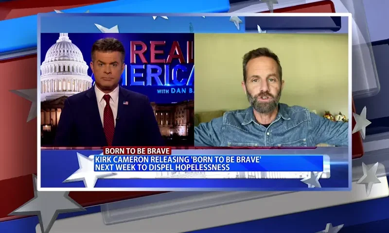 Video still from Real America on One America News Network showing a split screen of the host on the left side, and on the right side is the guest, Kirk Cameron.