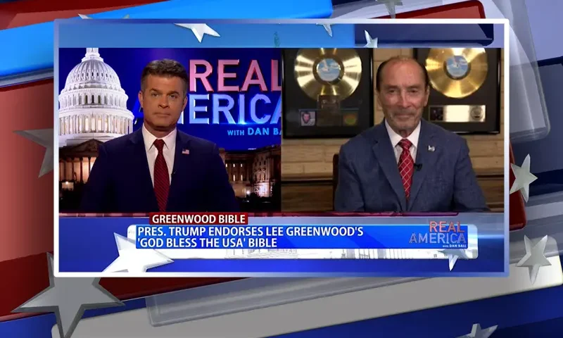 Video still from Real America on One America News Network showing a split screen of the host on the left side, and on the right side is the guest, Lee Greenwood.
