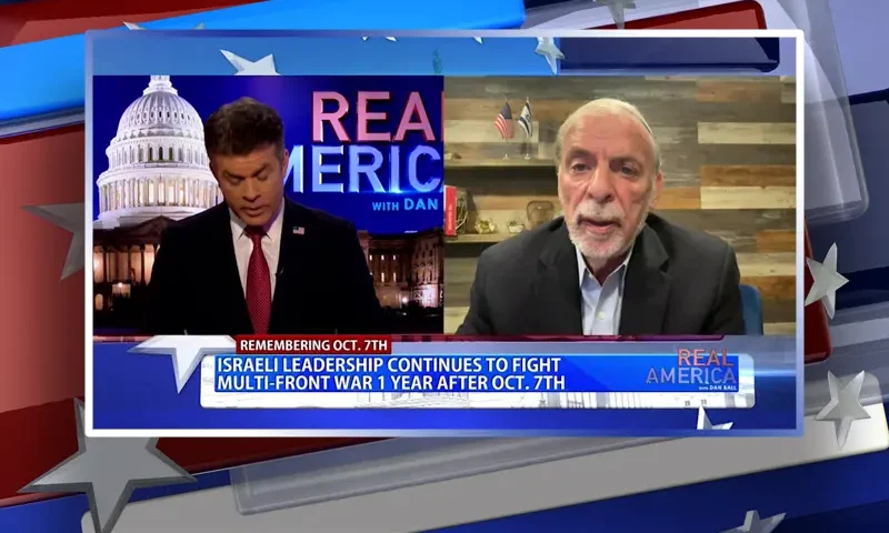Video still from Real America on One America News Network showing a split screen of the host on the left side, and on the right side is the guest, Dov Hikind.