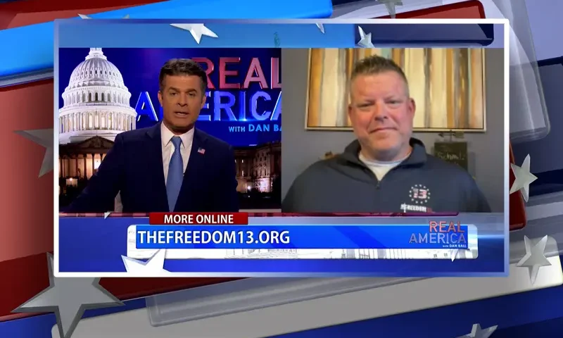 Video still from Real America on One America News Network showing a split screen of the host on the left side, and on the right side is the guest, Mark Schmitz.