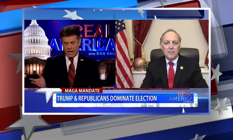 Video still from Real America on One America News Network showing a split screen of the host on the left side, and on the right side is the guest, Rep. Andy Biggs.