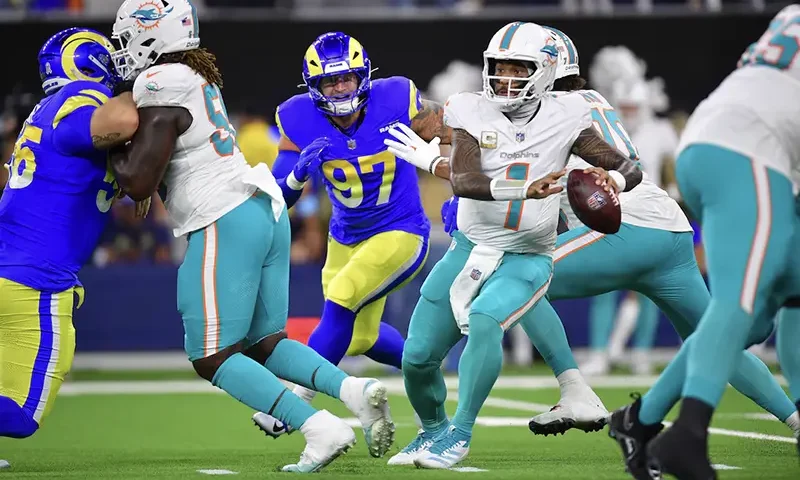 Miami Dolphins quarterback Tua Tagovailoa (1) moves out to pass as Los Angeles Rams linebacker Michael Hoecht (97) moves in during the first half at SoFi Stadium. Mandatory Credit: Gary A. Vasquez-Imagn Images