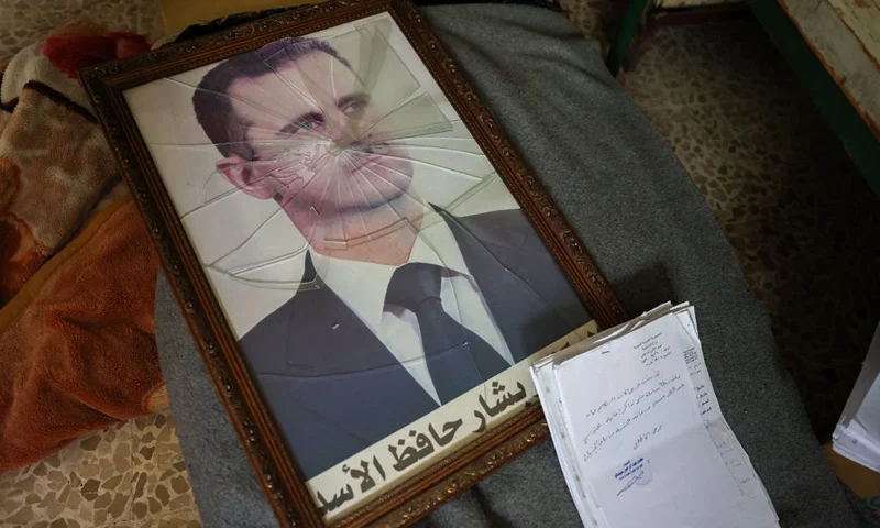 TOPSHOT - A portrait of Syrian President Bashar al-Assad is pictured with its frame broken, in a Syrian regime's Political Security Branch facility on the outskirts of the central city of Hama, following the capture of the area by anti-government forces, on December 7, 2024. Syria's embattled government said on December 7 it was setting up a ring of steel around Damascus, state media reported, as rebels on a lightning advance said they were bearing down on the city. The leader of Hayat Tahrir al-Sham (HTS), the Islamist group which has headed the assault, told fighters to prepare to take Damascus, just over a week into a renewed offensive in the long dormant conflict. (Photo by OMAR HAJ KADOUR / AFP) (Photo by OMAR HAJ KADOUR/AFP via Getty Images)