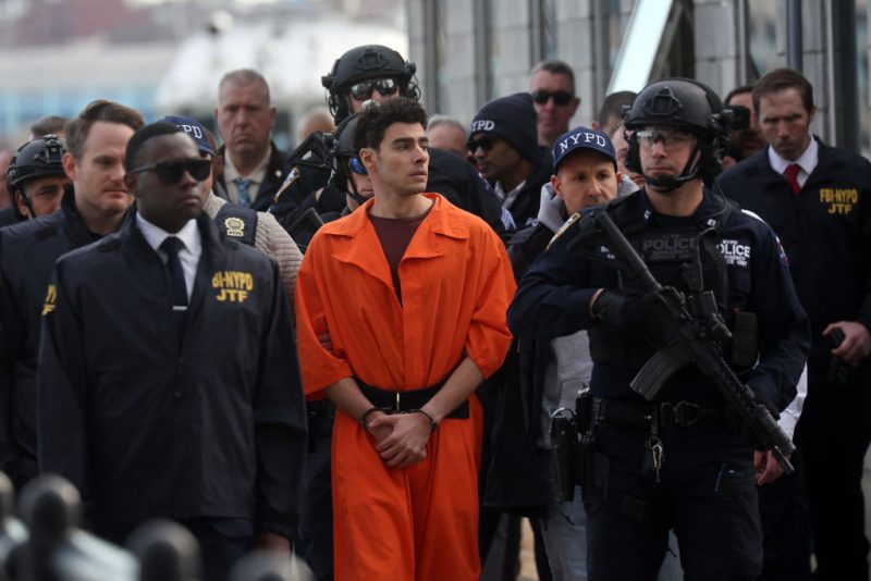 NEW YORK, NEW YORK - DECEMBER 19: Luigi Mangione, suspect in the killing of UnitedHealthcare CEO Brian Thompson in New York City, arrives at a heliport with members of the NYPD on December 19, 2024 in New York City. The 26-year-old was arrested in Pennsylvania on December 9 after being spotted at a McDonald's in Altoona amid a national manhunt. Mangione also appeared in a Pennsylvania court on forgery and firearms charges today, where he waived extradition to New York after being indicted on 11 charges including first-degree murder in furtherance of terrorism. (Photo by Spencer Platt/Getty Images)