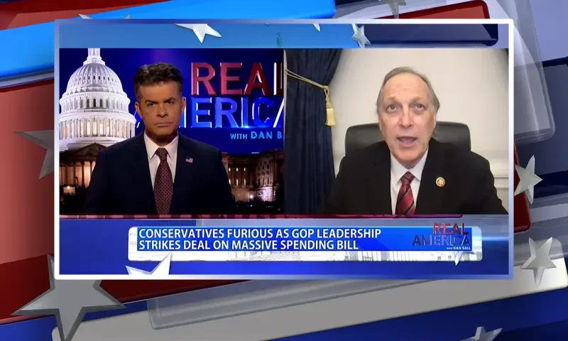 Video still from Real America on One America News Network showing a split screen of the host on the left side, and on the right side is the guest, Rep. Andy Biggs.