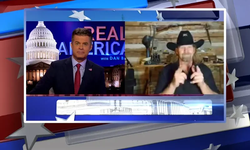 Video still from Real America on One America News Network showing a split screen of the host on the left side, and on the right side is the guest, Michael Carmichael.