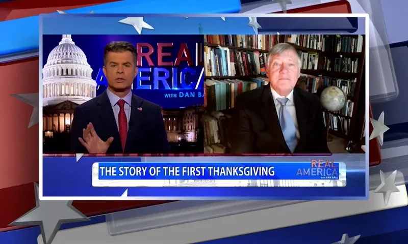 Video still from Real America on One America News Network showing a split screen of the host on the left side, and on the right side is the guest, Jerry Newcombe.