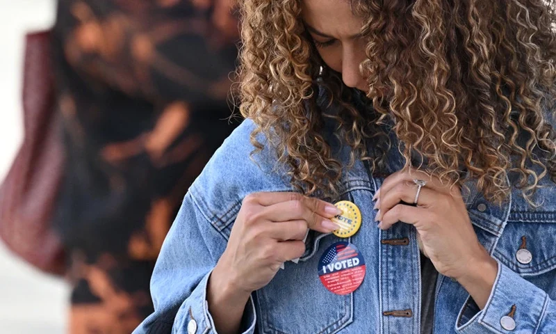 A young woman attaches a pin to her jacket after voting at a mobile outdoor vote center at SoFi Stadium in Los Angeles, California, on Election Day, November 5, 2024. (Photo by Robyn Beck / AFP) (Photo by ROBYN BECK/AFP via Getty Images)