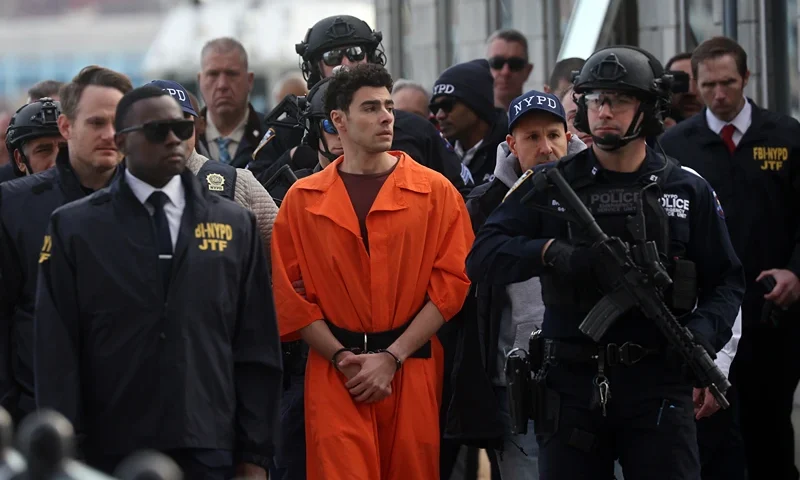 NEW YORK, NEW YORK - DECEMBER 19: Luigi Mangione, suspect in the killing of UnitedHealthcare CEO Brian Thompson in New York City, arrives at a heliport with members of the NYPD on December 19, 2024 in New York City. The 26-year-old was arrested in Pennsylvania on December 9 after being spotted at a McDonald's in Altoona amid a national manhunt. Mangione also appeared in a Pennsylvania court on forgery and firearms charges today, where he waived extradition to New York after being indicted on 11 charges including first-degree murder in furtherance of terrorism. (Photo by Spencer Platt/Getty Images)