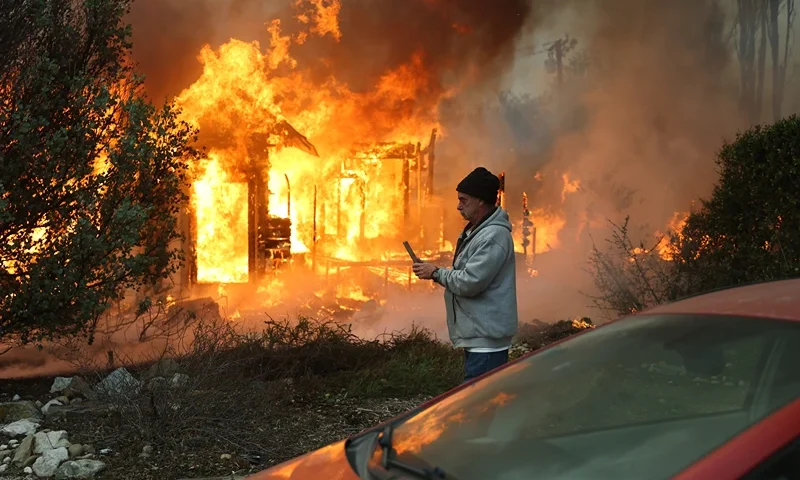 ALTADENA, CALIFORNIA - JANUARY 08: A person walks past a home burning during the Eaton Fire on January 8, 2025 in Altadena, California. Over 1,000 structures have burned, with two people dead, in wildfires fueled by intense Santa Ana Winds across L.A. County. (Photo by Mario Tama/Getty Images)
