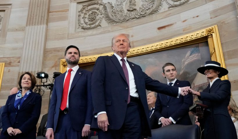 US President Donald Trump, center, holds the hand of his wife Melania Trump, far right, as their son Barron Trump, US Vice President JD Vance, and Sen. Amy Klobuchar, D-Minn., far left, look on after taking the oath of office during the 60th Presidential Inauguration in the Rotunda of the US Capitol in Washington, DC. Donald Trump takes office for his second term as the 47th president of the United States. (Photo by Morry Gash / POOL / AFP) (Photo by MORRY GASH/POOL/AFP via Getty Images)