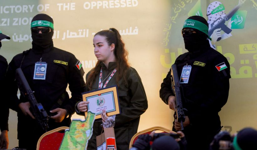 Hamas militants escort Isreali hostage Agam Berger (C) on a stage before handing her over to a Red Cross team in Jabalia on January 30, 2025, as part of their third hostage-prisoner exchange. (Photo by Saeed Jaras / Middle East Images / Middle East Images via AFP) (Photo by SAEED JARAS/Middle East Images/AFP via Getty Images)