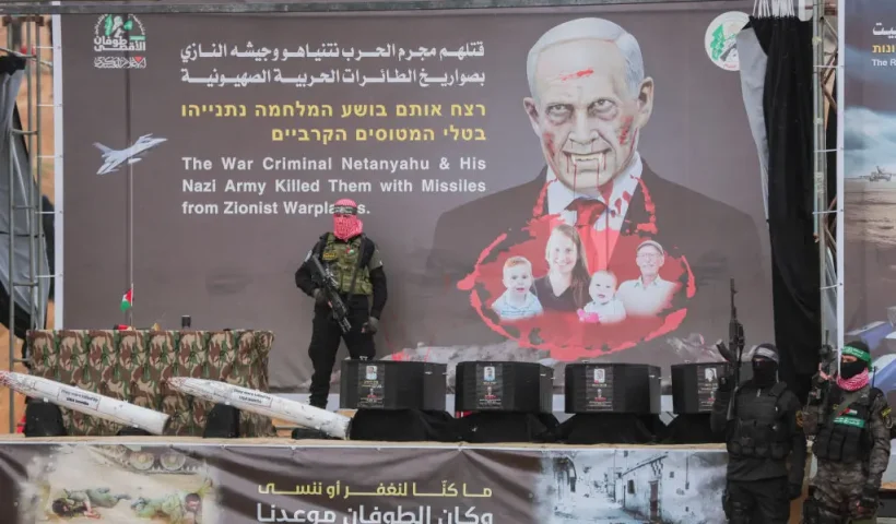 Armed Palestinian militants stand next to the coffins on stage before handing over the bodies of four Israeli hostages to the Red Cross in Khan Yunis in the southern Gaza on February 20, 2025. Hamas handed over on February 20 coffins believed to contain the bodies of four Israeli hostages, including those of the Bibas family who became symbols of the ordeal that has gripped Israel since the Gaza war began. The transfer of the bodies is the first by Hamas since its October 7, 2023 attack on Israel triggered the war, and is taking place under a fragile ceasefire that has seen living hostages exchanged for Palestinians held in Israeli prisons. (Photo by Abood Abusalama / Middle East Images / Middle East Images via AFP) (Photo by ABOOD ABUSALAMA/Middle East Images/AFP via Getty Images)