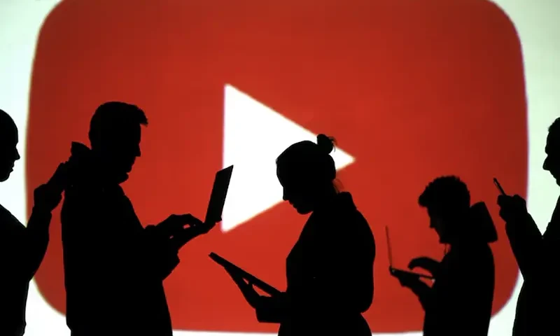 Silhouettes of laptop and mobile device users are seen next to a screen projection of Youtube logo in this picture illustration taken March 28, 2018. REUTERS/Dado Ruvic/Illustration/File Photo