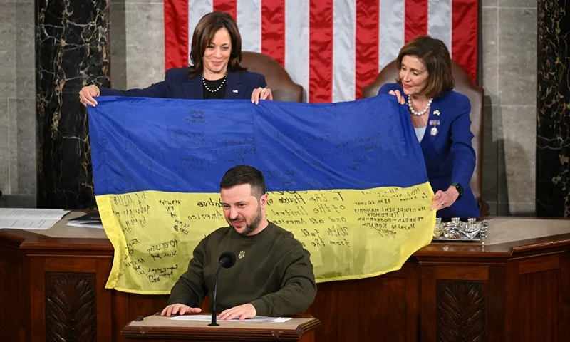 TOPSHOT - Ukraine's President Volodymyr Zelensky addresses the US Congress as US Vice President Kamala Harris (L) and US House Speaker Nancy Pelosi (D-CA) hold a Ukrainian national flag that Zelensky gave them at the US Capitol in Washington, DC on December 21, 2022. Zelensky is in Washington to meet with US President Joe Biden and address Congress -- his first trip abroad since Russia invaded in February. (Photo by Mandel NGAN / AFP) (Photo by MANDEL NGAN/AFP via Getty Images)