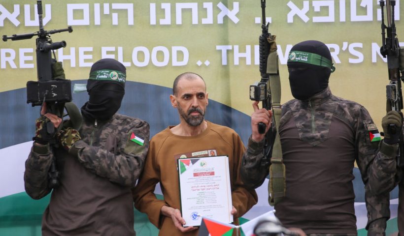 TOPSHOT - CORRECTION / Hamas fighters escort Israeli hostage Eli Sharabi on a stage before handing him over to a Red Cross team in Deir el-Balah, central Gaza, on February 8, 2025. Hamas militants handed over three Israeli hostages on February 8, as part of the fifth exchange under a fragile Gaza ceasefire, with 183 prisoners held by Israel due to be released later in the day. (Photo by Eyad BABA / AFP) / "The erroneous mention[s] appearing in the metadata of this photo by Eyad BABA has been modified in AFP systems in the following manner: [Eli Sharabi] instead of [Or Levy]. Please immediately remove the erroneous mention[s] from all your online services and delete it (them) from your servers. If you have been authorized by AFP to distribute it (them) to third parties, please ensure that the same actions are carried out by them. Failure to promptly comply with these instructions will entail liability on your part for any continued or post notification usage. Therefore we thank you very much for all your attention and prompt action. We are sorry for the inconvenience this notification may cause and remain at your disposal for any further information you may require." (Photo by EYAD BABA/AFP via Getty Images)