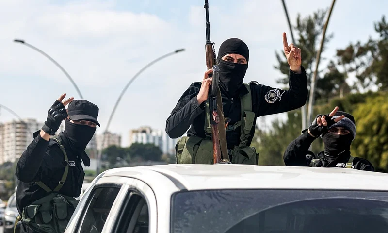 Security forces loyal to the interim Syrian government gesture as they ride in the back of a vehicle moving along a road in Syria's western city of Latakia on March 9, 2025. Syria's interim President Ahmed al-Sharaa called for national unity and peace on March 9, amid growing international backlash following the killing of civilians along the country's coast in the worst violence since the overthrow of former president Bashar al-Assad, in the heartland of the Alawite minority to which the latter belongs. (Photo by OMAR HAJ KADOUR / AFP) (Photo by OMAR HAJ KADOUR/AFP via Getty Images)
