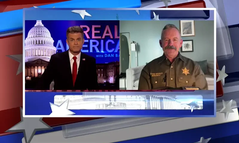 Video still from Real America on One America News Network showing a split screen of the host on the left side, and on the right side is the guest, Chad Bianco.