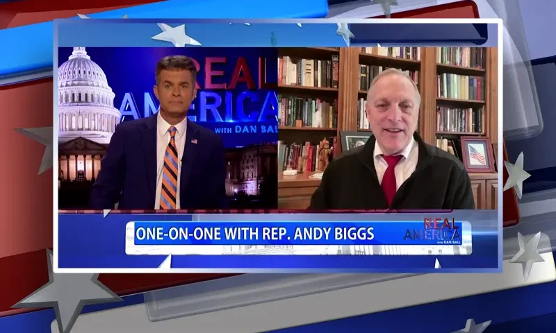 Video still from Real America on One America News Network showing a split screen of the host on the left side, and on the right side is the guest, Rep. Andy Biggs.