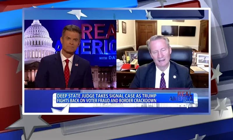Video still from Real America on One America News Network showing a split screen of the host on the left side, and on the right side is the guest, Rep. Tim Burchett.