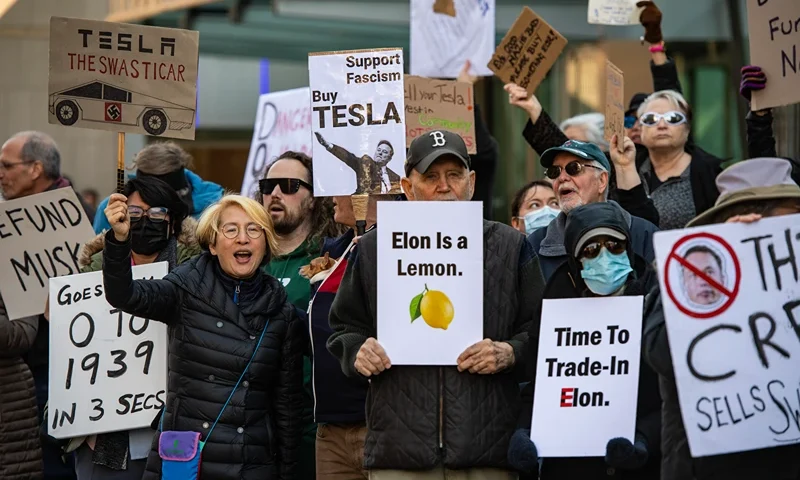 Protesters hold signs and sing chants during a protest against Elon Musk and his Tesla car company outside the Tesla dealership in Boston, Massachusetts on March 15, 2025. US President Donald Trump's senior advisor Elon Musk is leading the so-called Department of Government Efficiency (DOGE), which has cut thousands of government jobs and upended agencies, prompting numerous court challenges. (Photo by Joseph Prezioso / AFP) (Photo by JOSEPH PREZIOSO/AFP via Getty Images)