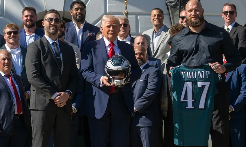 TOPSHOT - US President Donald Trump holds up a helmet, flanked by Philadelphia Eagles' tackle #65 Lane Johnson (R) and Philadelphia Eagles head coach Nick Sirianni (L), as he hosts an event celebrating the Philadelphia Eagles, 2025 Super Bowl champions, at the White House on April 28, 2025, in Washington, DC. The Eagles defeated the defending champion Kansas City Chiefs 40-22 in Super Bowl LIX, held in New Orleans, Louisiana on February 9, 2025. (Photo by Jim WATSON / AFP) (Photo by JIM WATSON/AFP via Getty Images)