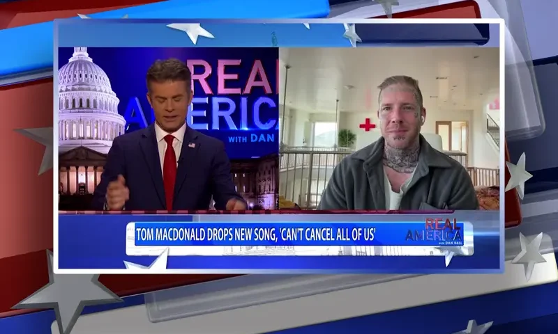 Video still from Real America on One America News Network showing a split screen of the host on the left side, and on the right side is the guest, Tom MacDonald.