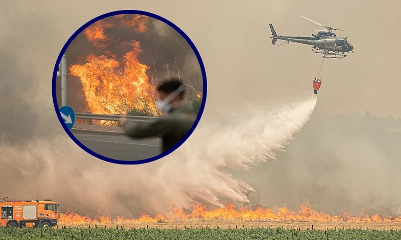 (L) Facemasked Israeli police officer stands near one of the spots of the wildfire that burns in the vicinity of Jerusalem, Israel, on April 30, 2025. (Photo by Ori Aviram / Middle East Images / Middle East Images via AFP) (Photo by ORI AVIRAM/Middle East Images/AFP via Getty Images) / (Background) An Israeli firefighting helicopter pours water on one of the fire spots of the wildfires that burn around Jerusalem, Israel on April 30, 2025. (Photo by Ori Aviram / Middle East Images / Middle East Images via AFP) (Photo by ORI AVIRAM/Middle East Images/AFP via Getty Images)